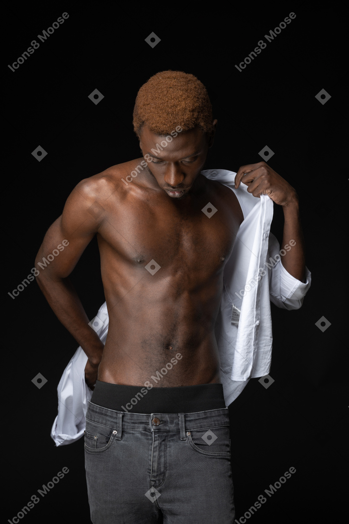 Close-up un joven africano poniéndose una camisa en la oscuridad