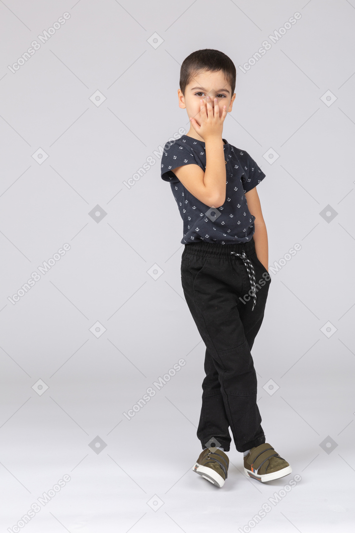 Vue de face d'un garçon mignon dans des vêtements décontractés couvrant la bouche avec la main