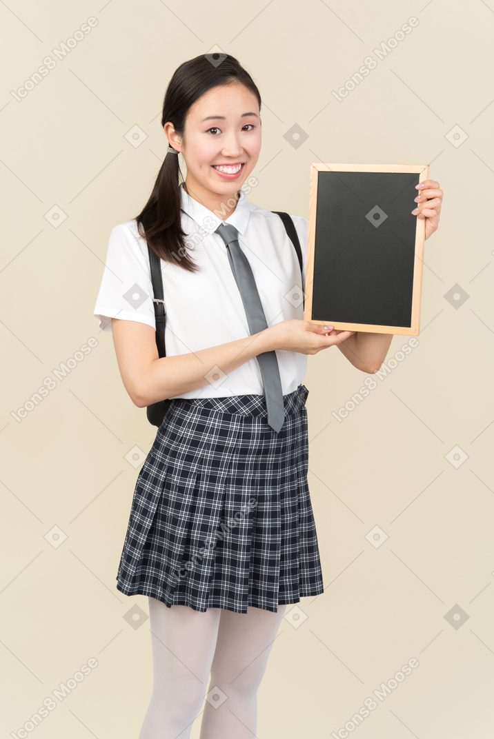 Sorrindo menina asiática da escola segurando pequena lousa