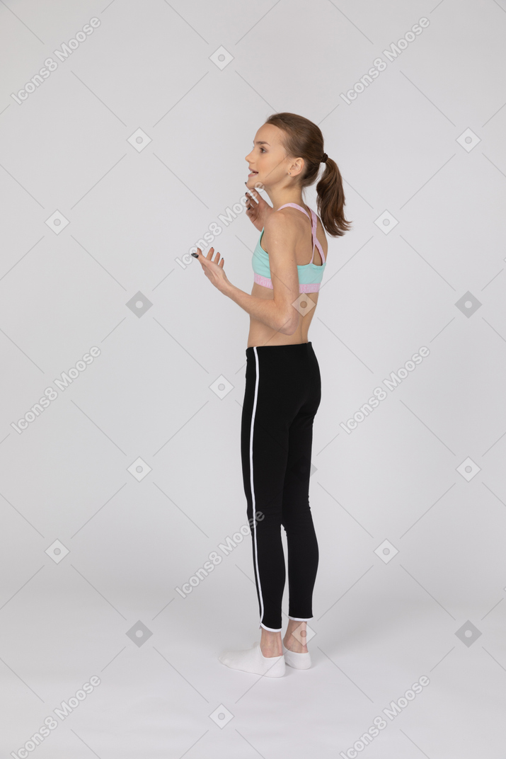 Vista posterior de tres cuartos de una jovencita en ropa deportiva levantando las manos y mirando a un lado