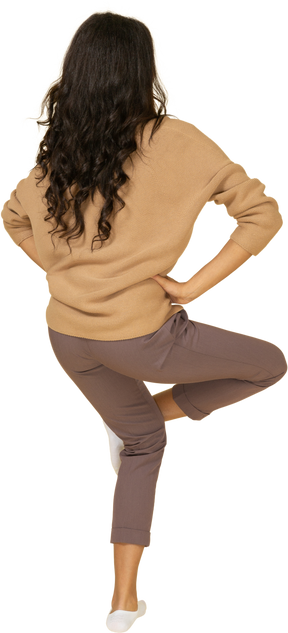 Вид сзади в три четверти темнокожей молодой девушки, поднимающей ногу и кладущей руки на бедра