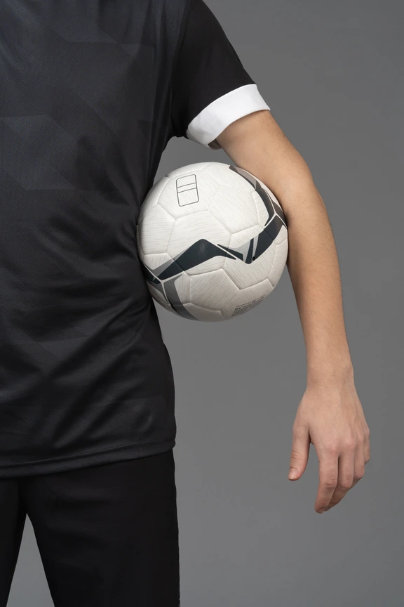 Football player with arms raised holding ball on black background