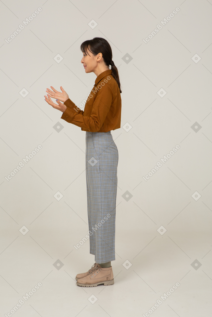 Vista laterale di una giovane donna asiatica in calzoni e camicetta che alza le mani