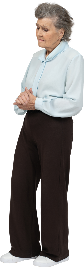 Foto di Vista di tre quarti di una donna anziana scontenta in camicetta e  pantaloni che si tengono per mano e guardano in basso