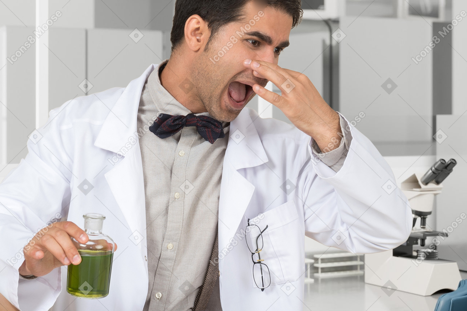 A man in a lab coat holding a glass of green liquid and closing his nose