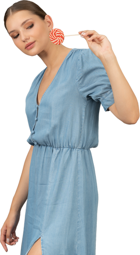 Vista di tre quarti di una giovane donna in abito blu che tiene un lecca-lecca