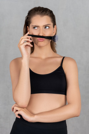 Woman with makeup brush between lips and nose as mustache