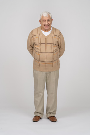 Вид спереди на счастливого старика в повседневной одежде, стоящего с руками за спиной