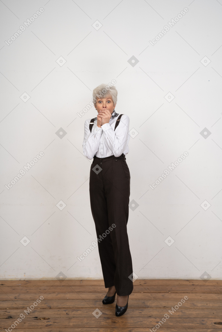 Front view of a horrified old lady in office clothing biting fingers