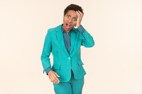 Black woman with a short haircut, wearing all blue, standing against a plain pastel background, looking emotional