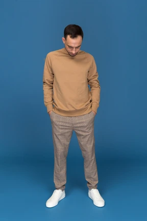 Young man standing with hands in pockets and looking down