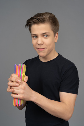 Shy young man holding a pile of plastic straws