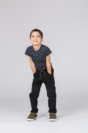 Vista frontal de un niño feliz en ropa casual posando con las manos en los bolsillos y mirando a la cámara