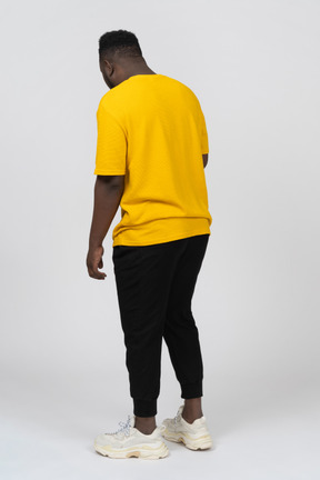 一个身穿黄色 t 恤、站着不动的黑皮肤年轻男子的四分之三后视图