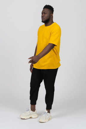 Dreiviertelansicht eines jungen gestikulierenden dunkelhäutigen mannes in gelbem t-shirt, der etwas erklärt