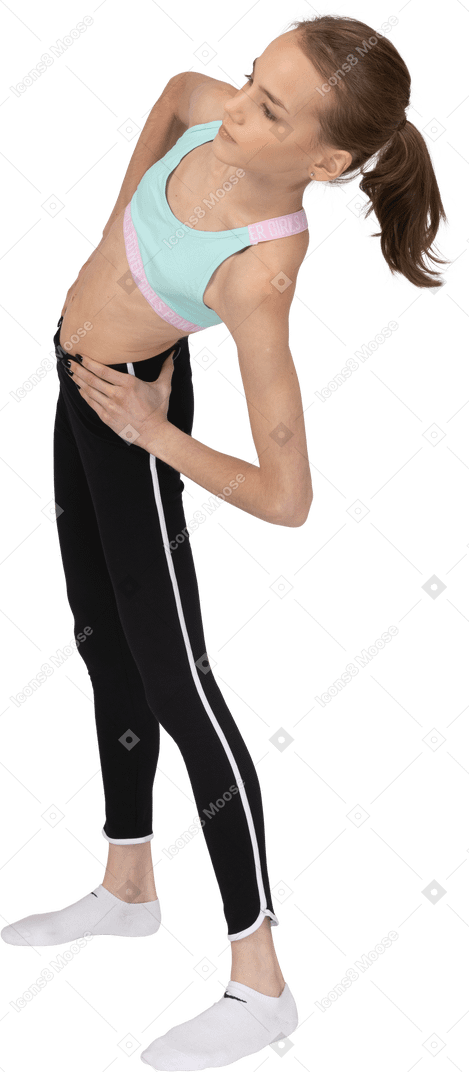 Vista posteriore di tre quarti di una ragazza adolescente in abbigliamento sportivo che mette le mani sui fianchi mentre si inclina a sinistra