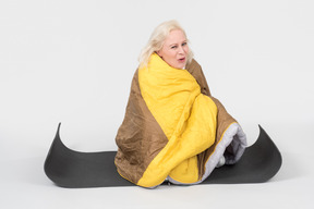 Mature woman sitting on yoga mat wrapped in blanket