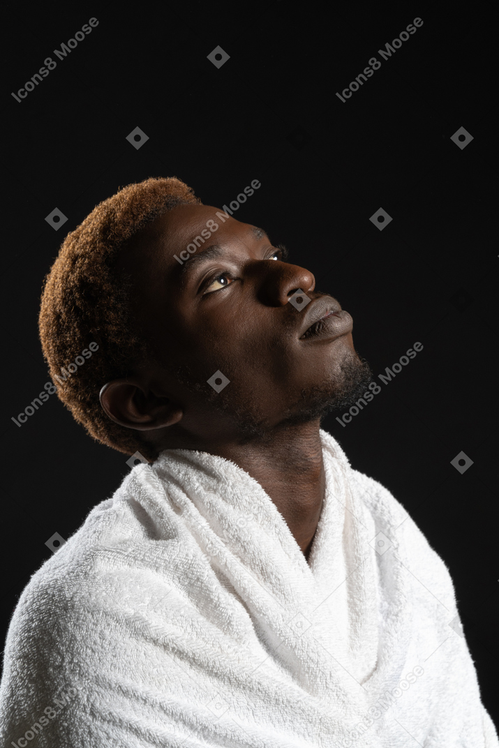 Um jovem em uma toalha olhando para o lado sonhadoramente