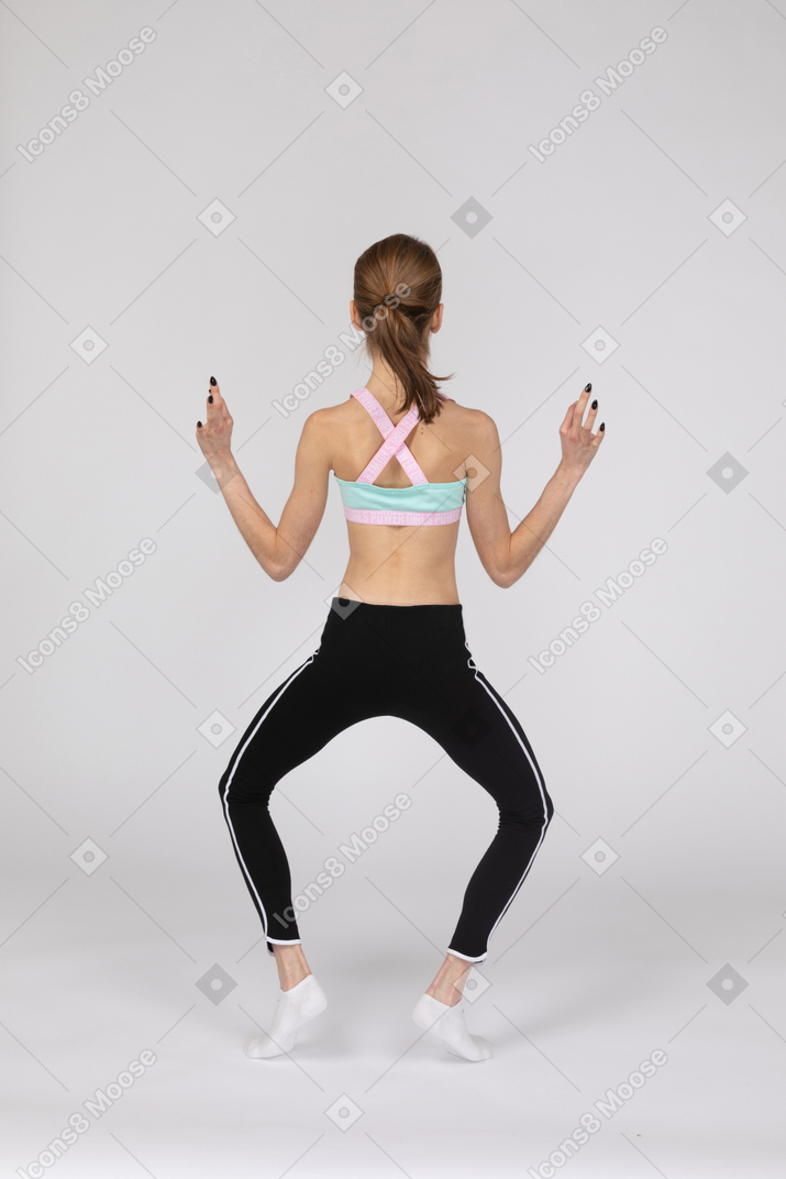 Vista traseira de uma adolescente em roupas esportivas separando as pernas