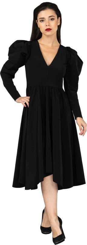 Vista frontal de una joven en un vestido negro poniendo la mano en la cadera