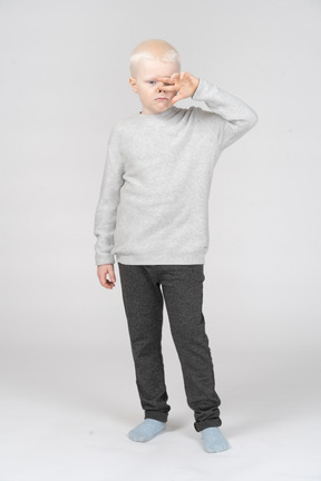 Front view of a grimacing kid boy touching nose