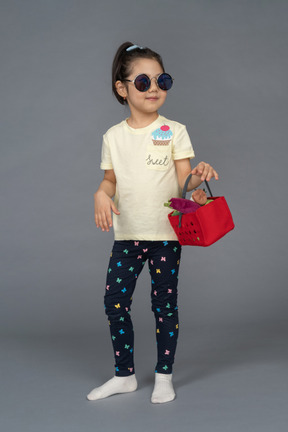 Retrato de uma menina em óculos de sol segurando uma cesta de compras