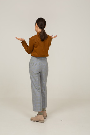Vista posterior de tres cuartos de una joven mujer asiática en calzones y blusa levantando las manos