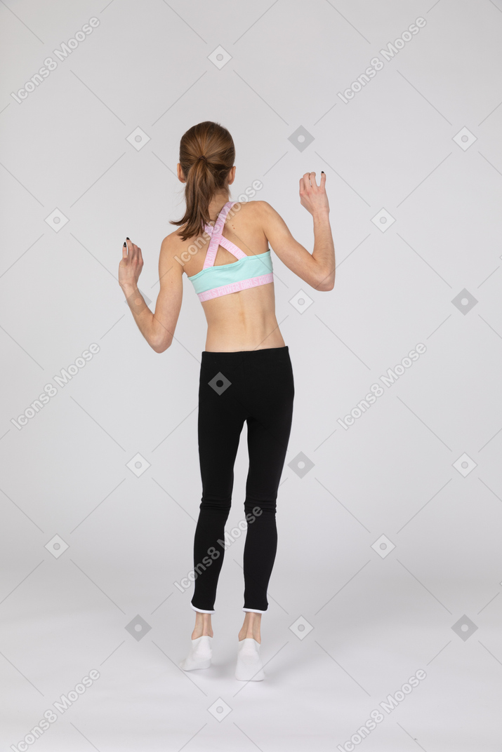 Back view of a teen girl in sportswear raising hands while balancing