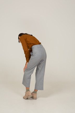 Three-quarter back view of a young asian female in breeches and blouse leaning forward