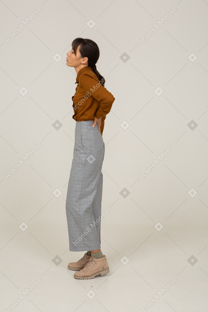 Вид сбоку молодой азиатской женщины в бриджах и блузке, касающейся спины