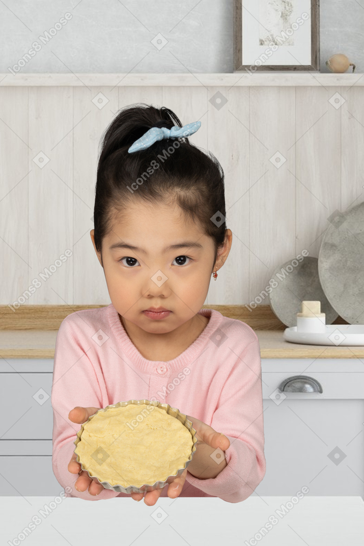A little girl holding a tart pan with dough