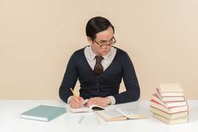 Young asian student in a sweater writing in a notebook