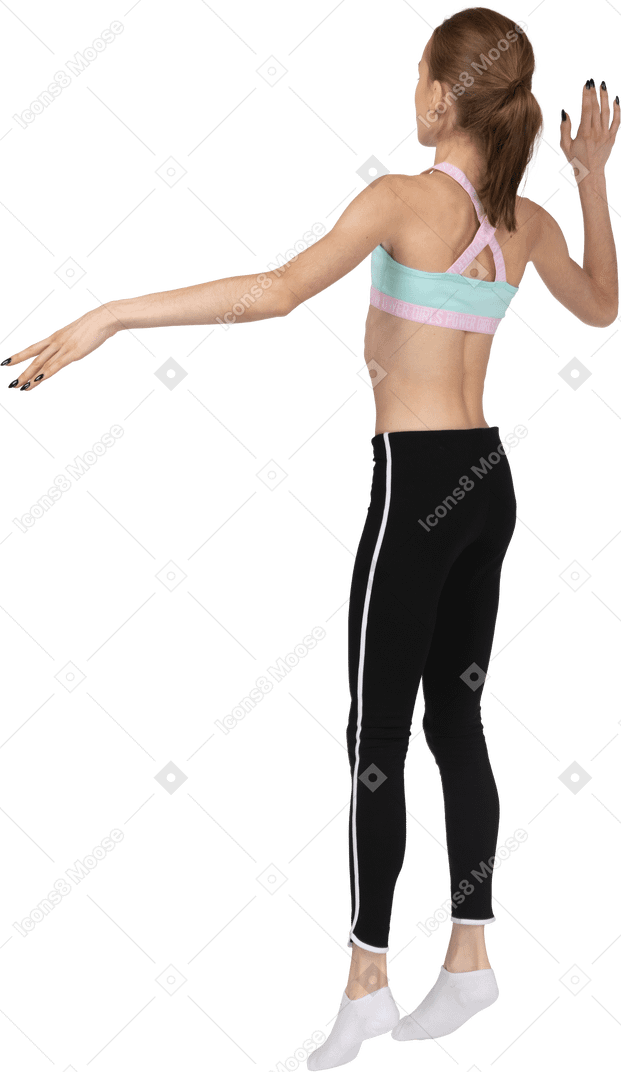 Vista traseira de três quartos de uma adolescente em roupas esportivas levantando a mão e pulando