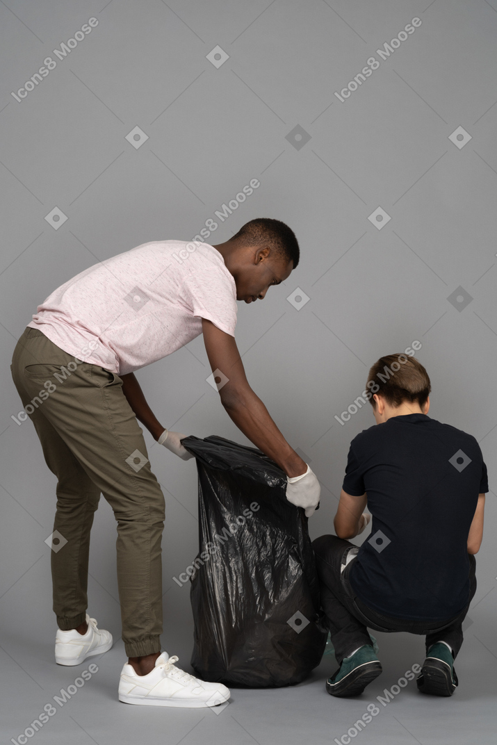 Two young men arranging a trash bag