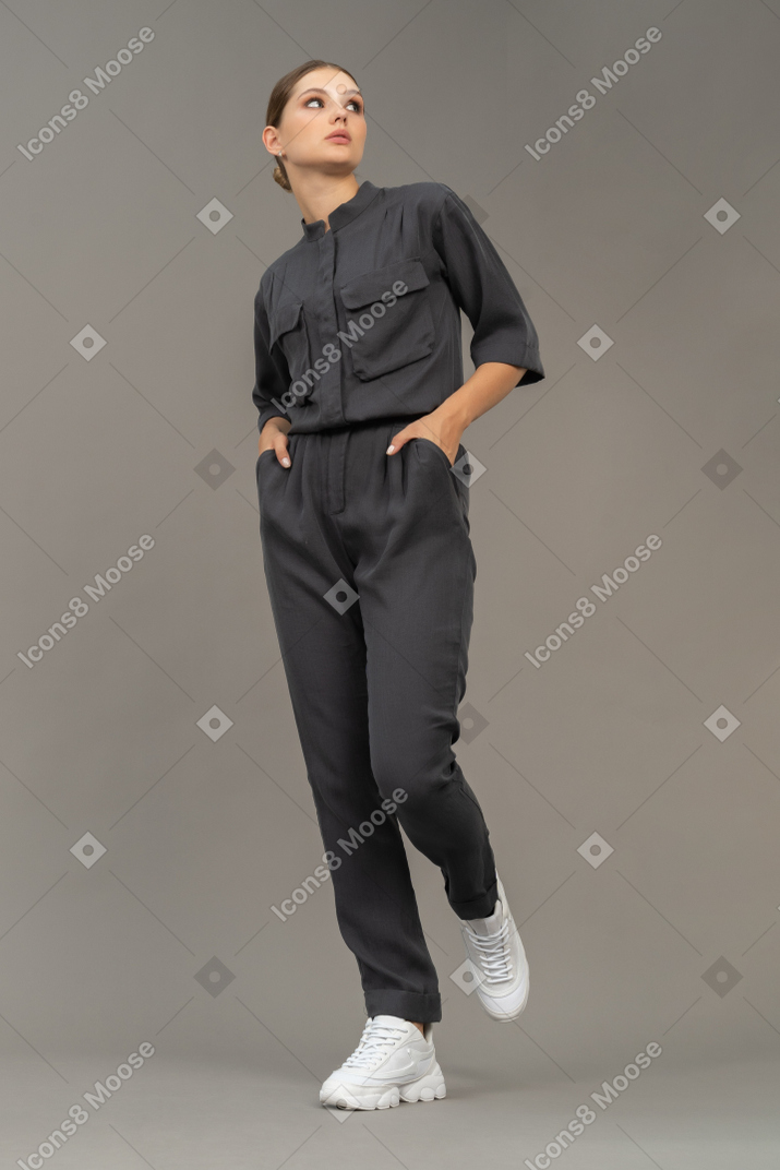 Front view of a walking young woman in a jumpsuit holding hands in pockets
