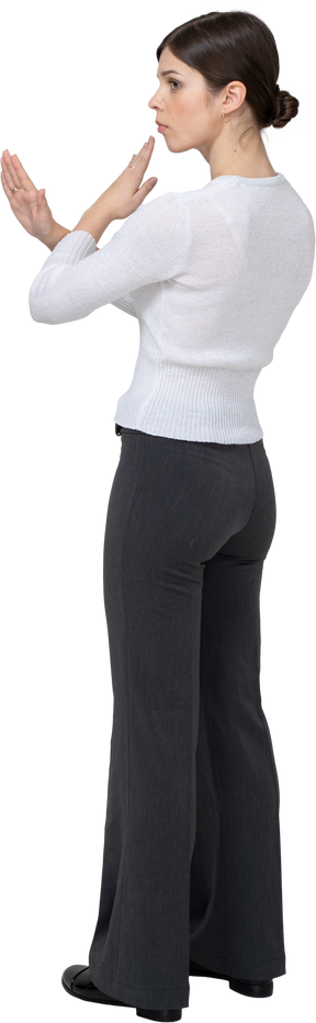 Three-quarter back view of a young woman in office clothing crossing arms
