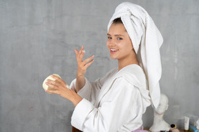 Smiling woman in bathrobe applying hand cream