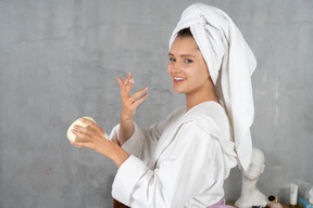 Femme souriante en peignoir appliquant de la crème pour les mains