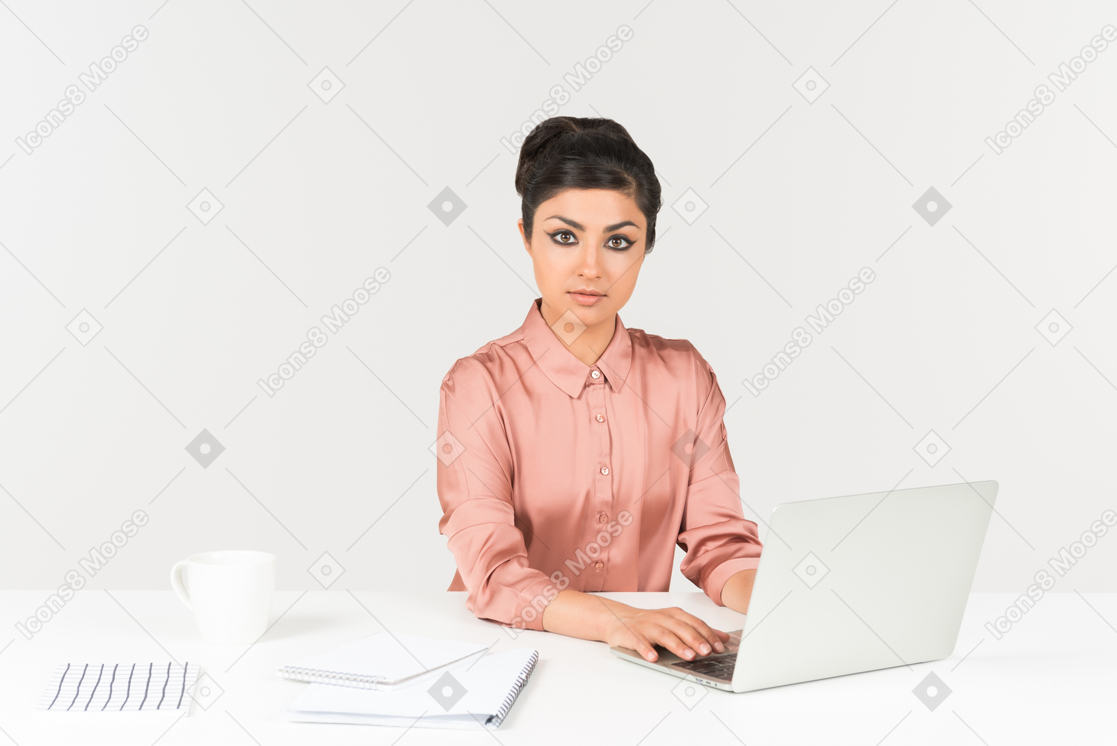 Young indian office worker working on laptop and looking right into camera