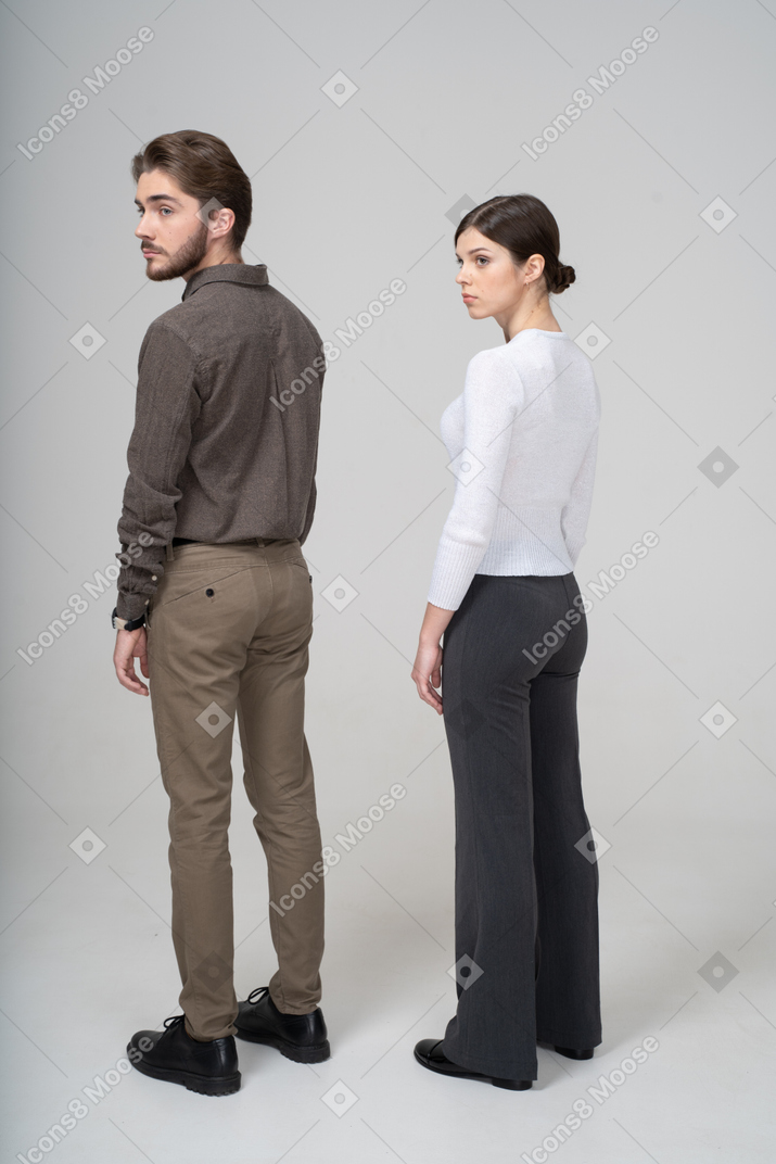 Three-quarter back view of a young couple in office clothing turning head