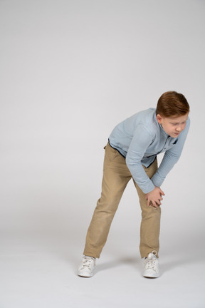Vista frontal de um menino se curvando e tocando o joelho dolorido