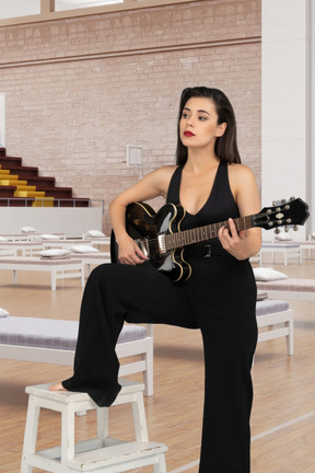 A woman leaning on a stool playing a guitar