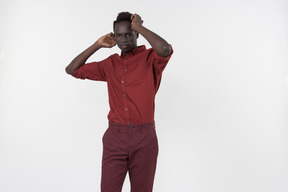 Un joven negro con una camisa roja con mangas enrolladas y pantalones rojo oscuro de pie solo sobre el fondo blanco.