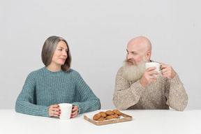 Pareja de ancianos sentados en la mesa y tomando café y galletas