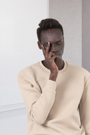 A man in a white sweater is holding his hand to his face