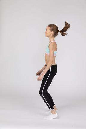 Side view of a teen girl in sportswear squatting and putting hands on hips