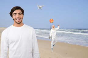 A man on a beach and another man fencing behind him
