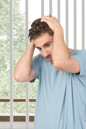 A man in a blue shirt is holding his head