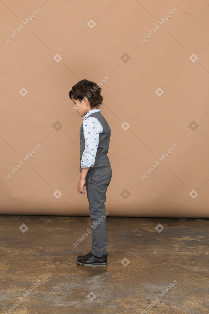 Cute boy in grey suit standing in profile and looking down