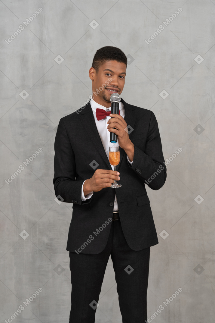 Uomo ben vestito con bicchiere di champagne e microfono che guarda l'obbiettivo